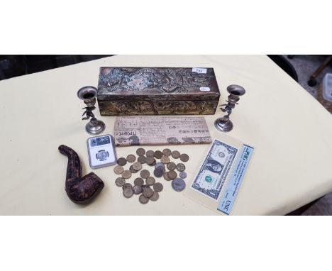 A metal box containing coins, uncirculated $1 US note, candlesticks featuring cherubs, cased pipe with hallmarked silver coll
