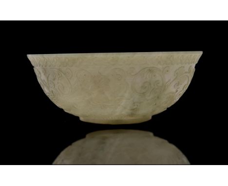 A Chinese celdon jade bowl, with rounded sides rising to an everted rim, the exterior carved in relief with lotus sprays, the