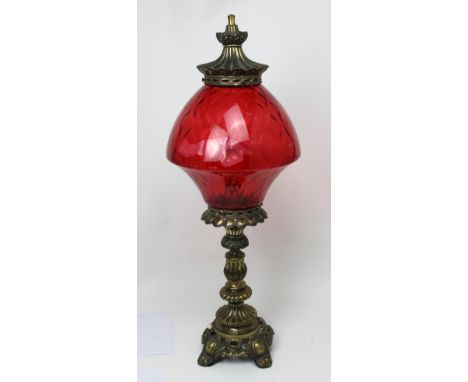 A large ornamental brass lamp with red glass shade, in the style of an oil lamp. CONDITION REPORT Some wear to the metal base