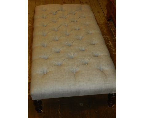 A Contemporary button back footstool, upholstered in stone linen, and raised on gun barrel legs and casters.