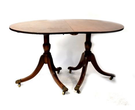 A Regency-style mahogany D-end twin pedestal dining table with one extra leaf, on tripod bases with outswept legs, brass lion