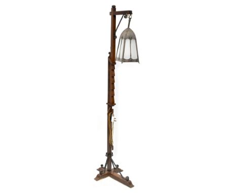 An early 20th century Arts &amp; Crafts standard lamp with wrought iron decoration to the base and top supporting a brass lan