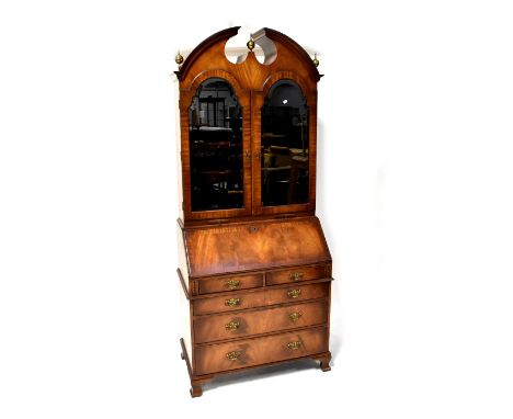 A reproduction mahogany bureau bookcase, the top with broken swan neck arched pediment above a pair of arched mirrored doors,