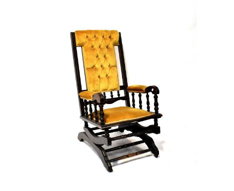 A 19th century American ebonised rocking chair with button-back mustard-coloured velour upholstery.