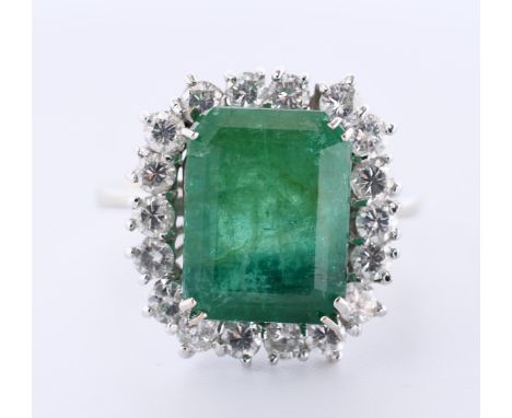 14 kt. Witgouden ring, centraal bezet met een emerald geslepen smaragd (12,4 x 9,5 mm) in een entourage van briljant geslepen