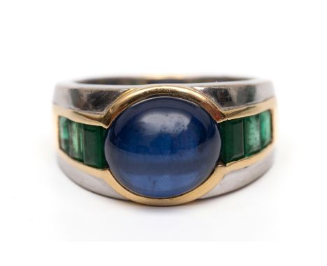 18 kt. wit- met geelgouden brede ring. Centraal bezet met een cabochon geslepen blauwe saffier met aan weerzijden een rij van