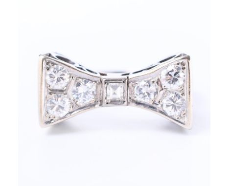 14 kt. Witgouden ring, in de vorm van een gestileerde strik. Centraal bezet met een carré geslepen diamant, de zijkanten elk 