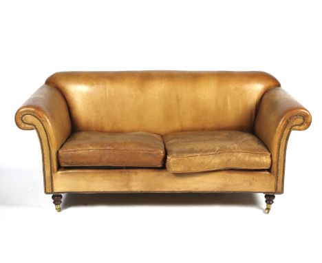 A two-seater tan leather sofa. With drop in seat cushions, on turned wooden legs and brass casters, L179cm x H82cm x D83cm