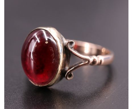 A vintage almandine cabochon ring, the oval stone (10 mm x 8 mm) bezel-set between the bifurcated scroll shoulders of a 9 ct 