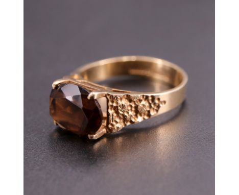 A 1970s smoky quartz and 9 ct gold ring, having an oval 10 x 8 mm stone, set on a plain four prong gallery between textured t