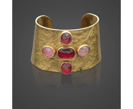 Robert GOOSSENS, circa 1990. Bracelet manchette en métal doré martelé.Agrémenté d'un motif de croix en pâte de verre rose.Sig