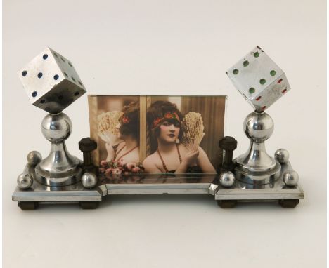 An Art Deco chromed photo frame, modelled with two dice, enamelled, raised on chess pawns, the cylindrical supports holding a