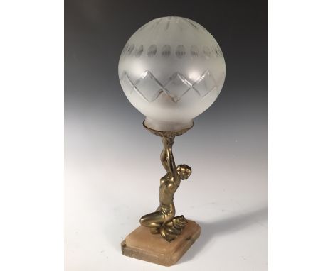 An Art Deco figural spelter table lamp, the gilt figure kneels holding a glass globular shade above, mounted on a stepped loz