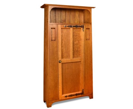 An Arts & Crafts single door oak wardrobe, the tapered cupboard with shelf top above a panelled door with copper strapwork hi