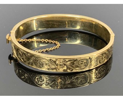 9CT ROSE GOLD HINGED HOLLOW BANGLE - engraved foliate decoration to one half, band width 10mm, with safety chain, 16.7grms