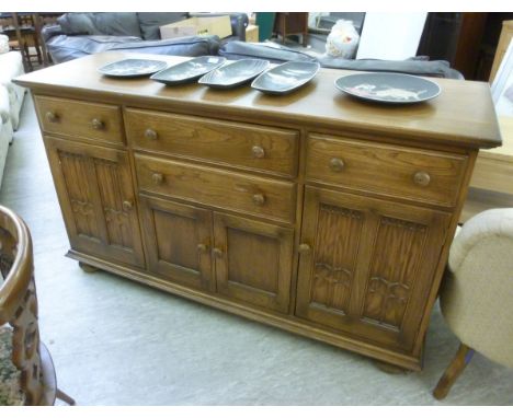 A modern Ercol 'Golden Dawn' sideboard, having three in-line drawers, over a central drawer and four panelled doors, raised o