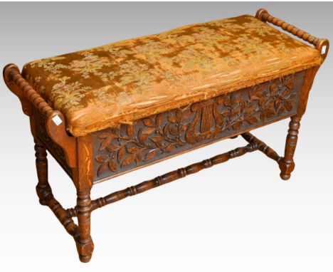 A Jacobean Revival carved oak rectangular bench / piano stool, bobbin turned handles above carved apron in high relief above 