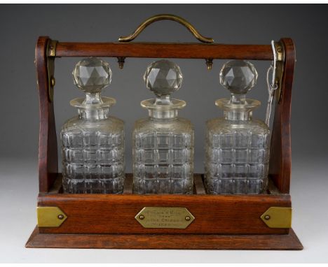 A Victorian EPNS bound oak tantalus complete with three glass spirit decanters and stoppers, the presentation plaque dated 18