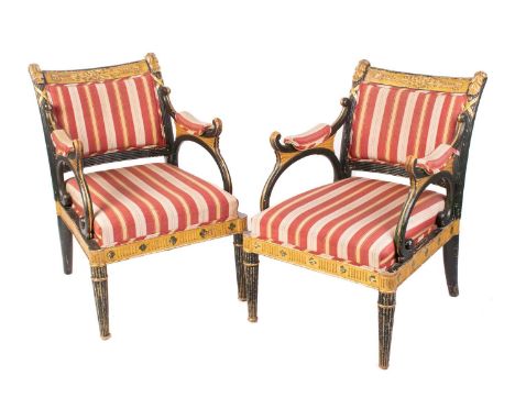 A pair of Regency and later painted and parcel gilt library armchairs with floral carved cresting rail flanked by tongues of 