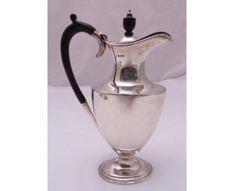 A hallmarked silver hot water jug of vase form with scroll handle, the domed hinged cover with urn finial on raised oval base