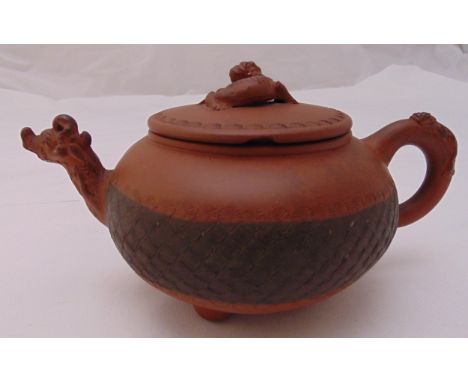 An unglazed Chinese terracotta teapot compressed cylindrical form, scroll handle and mask spout with pull off cover on three 