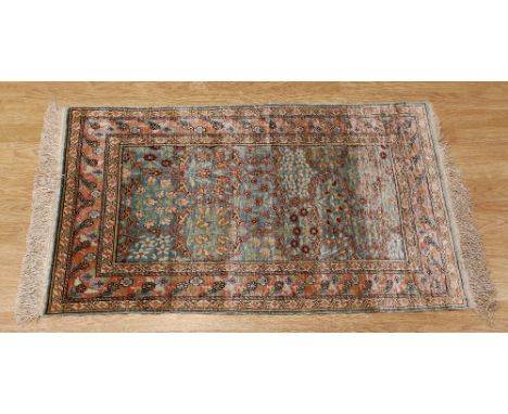 A Kashmir-type silk small mat with light blue ground and netted pattern, triple stripe flower head on repeat border and fring