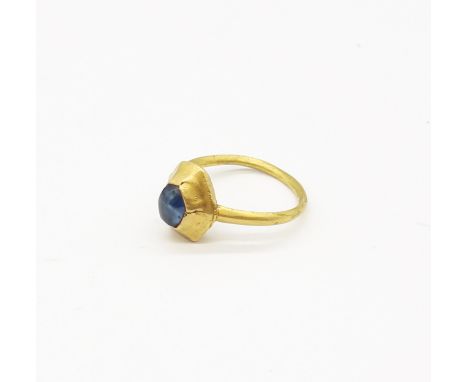 A 13th Century gold ring, with plain band hoop; the raised bezel with segmented sides forming a hexagon set with a cabochon s