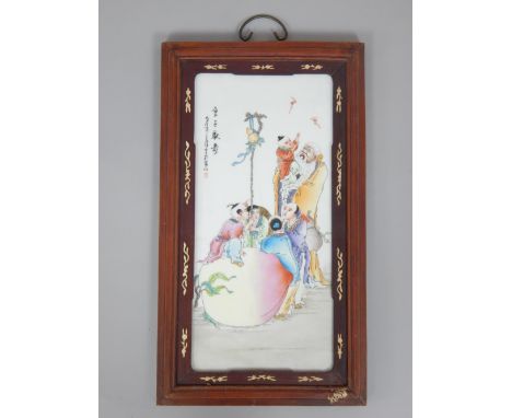 An early 20th century Chinese porcelain panel in a wooden frame, depicting a mythical scene of children playing on a giant pe