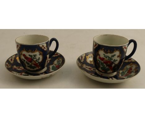 A pair of 18th century Worcester coffee cups and saucers, the scape blue ground decorated with reserve panels of fabulous bir