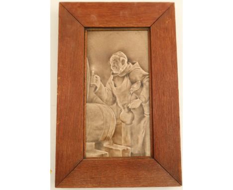 A brown glazed pottery tile, embossed with a monk and ale barrel, 11.5ins x 6ins, framed