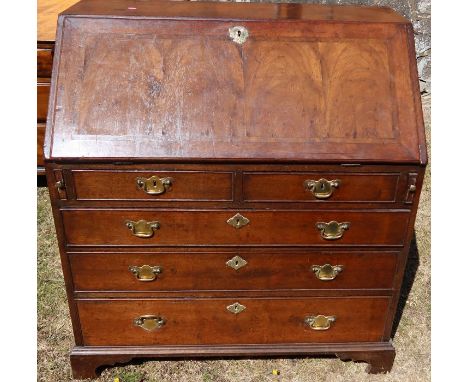An antique walnut and mahogany bureau, the sloping fall front opening to reveal cupboard, drawers, and pigeon holes, over two