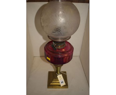 A Victorian table oil lamp with engraved opaque globular shade, above a cranberry tinted glass reservoir, mounted on a brass 