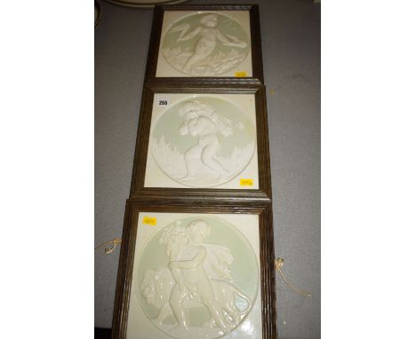 A set of three framed ceramic tiles, depicting putti in classical poses (maker unknown).