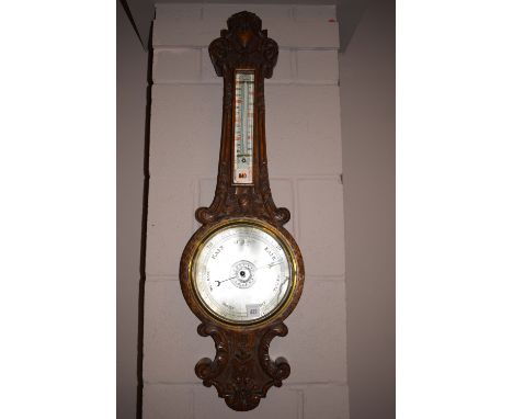 An early 20th Century aneroid barometer and thermometer, in ornate heavily carved and stained oak banjo pattern mount (glass 