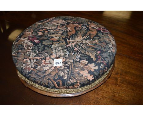 A Victorian footstool, covered in tapestry type material, raised on bun feet.