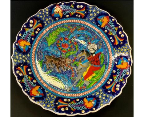 A Turkish charger, hand painted with a hunting scene in vibrant colours, marked made in Kutahya, turkey, signed Ahacet Sinon 