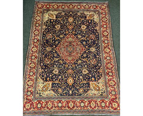 A Persian Kashan carpet, the diamond-shaped medallion within a field of scrolling flowering stems, in shades of red, orange, 