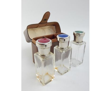 Three travelling perfume bottles within tan leather case, by B Altman & Co, with red, green and blue enamel tops, 10.5cm w