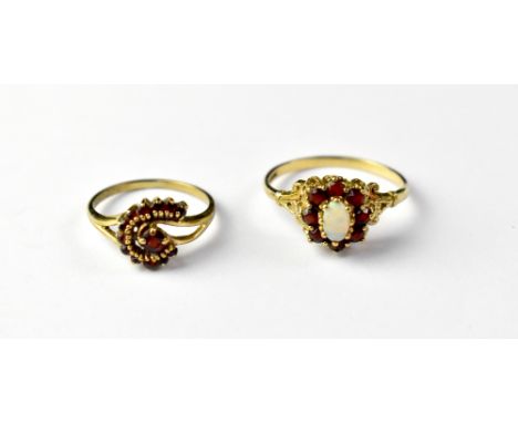 Two 9ct gold vintage-style red stone dress rings, one with a central oval white opal, raised above a border of small white st