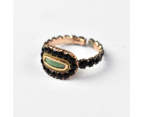 An early 19th century mourning ring, the small clear panel surrounded by an oval of black stones which continue around the sh