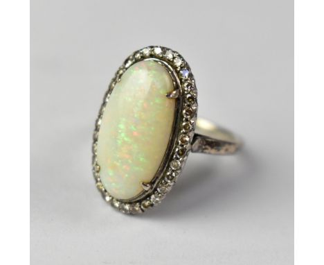 An opal and diamond ring with large white claw set opal within a border of tiny diamonds, with pierced open back, on an unmar