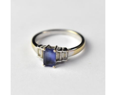 An 18ct white gold Art Deco inspired ring, with claw set square cut blue stone flanked by two graduated stepped diamond bague