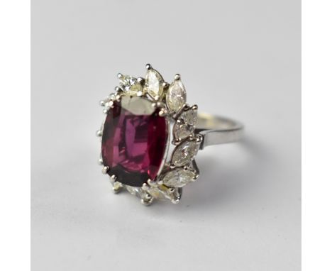 An 18ct white gold ruby (possibly synthetic) and diamond ring, the cushion cut claw set ruby raised above a border of twelve 