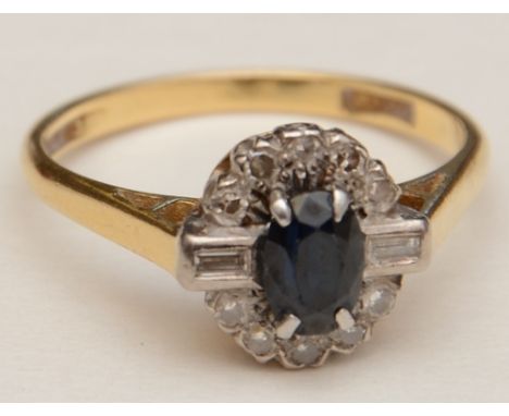 An 18ct gold and platinum sapphire and diamond cluster ring, the central oval cut sapphire mounted by two baguette cut diamon