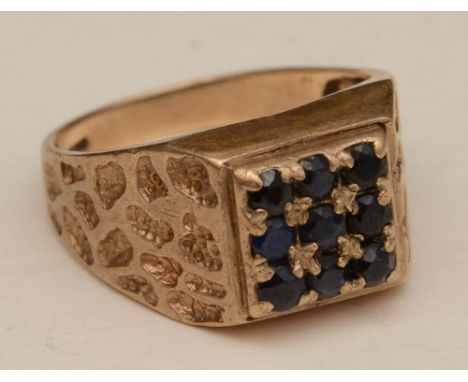 A 9ct gold and sapphire ring, the wide band set with nine round cut sapphires in square formation, with moulded relief decora