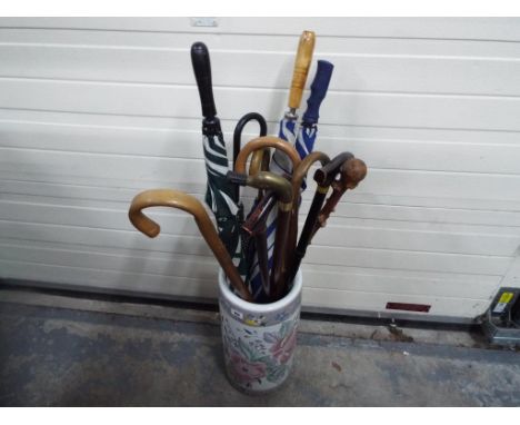 A ceramic umbrella stand with floral decoration containing seven walking sticks and five unbrellas
