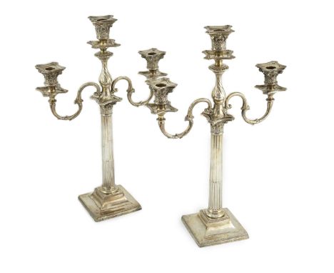 A matched pair of late 19th/early 20th century silver two branch, three light candelabrum, with scroll arms, on beaded square