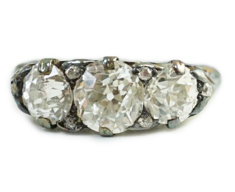 An antique gold, silver and graduated three stone diamond set ring, with diamond chip spacers and diamond chip set shoulders,