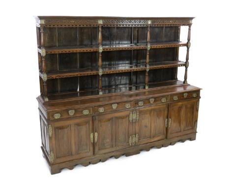 A rare Ceylonese Arts &amp; Crafts brass mounted teak dresser with scroll carved cornice and two open shelves over four long 