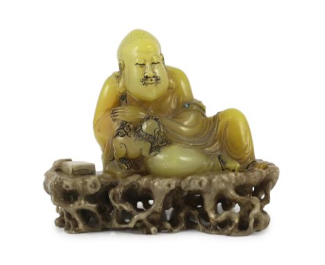 A Chinese soapstone seated group of a luohan and a lion-dog, on a soapstone stand, 18th century, the group of greenish yellow